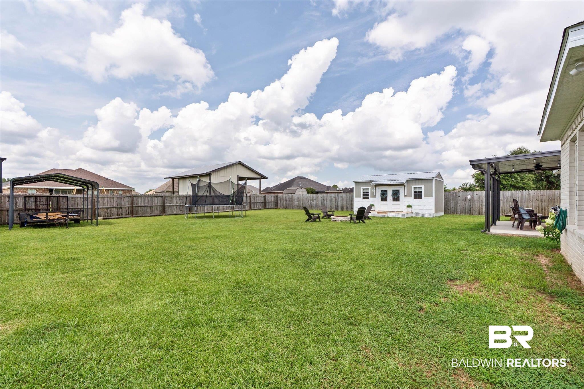 9074 Moses Way Theodore, AL 36582 - Photo 50 of 52 Expansive backyard featuring a manicured lawn, full privacy fencing, a covered patio with an outdoor fan, a detached storage shed, and an additional covered structure