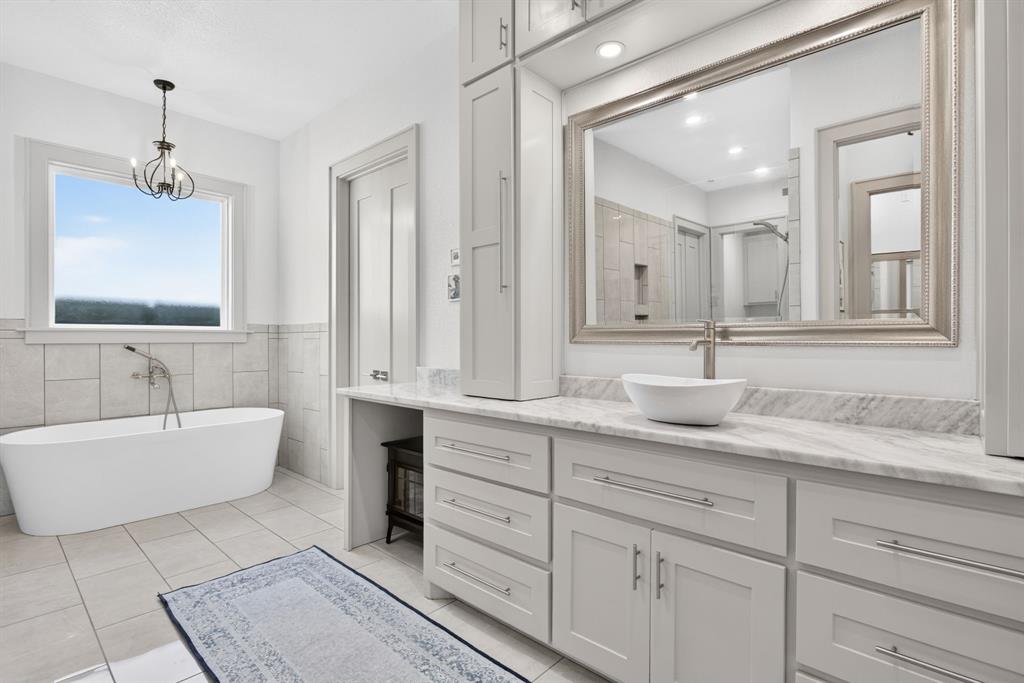 3008 Perkins Weatherford, TX 76088 - Photo 20 of 36 Bathroom featuring a freestanding soaking tub with floor-mounted tub filler, light-toned tile wainscoting, and a large vanity with a vessel sink, stone countertop, and extensive cabinetry