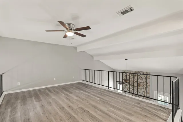 an empty room with wooden floor fan and windows