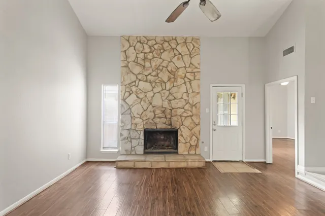 an empty room with wooden floor fireplace and windows