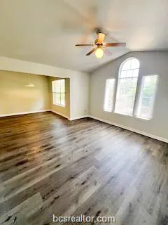 an empty room with wooden floor fan and windows