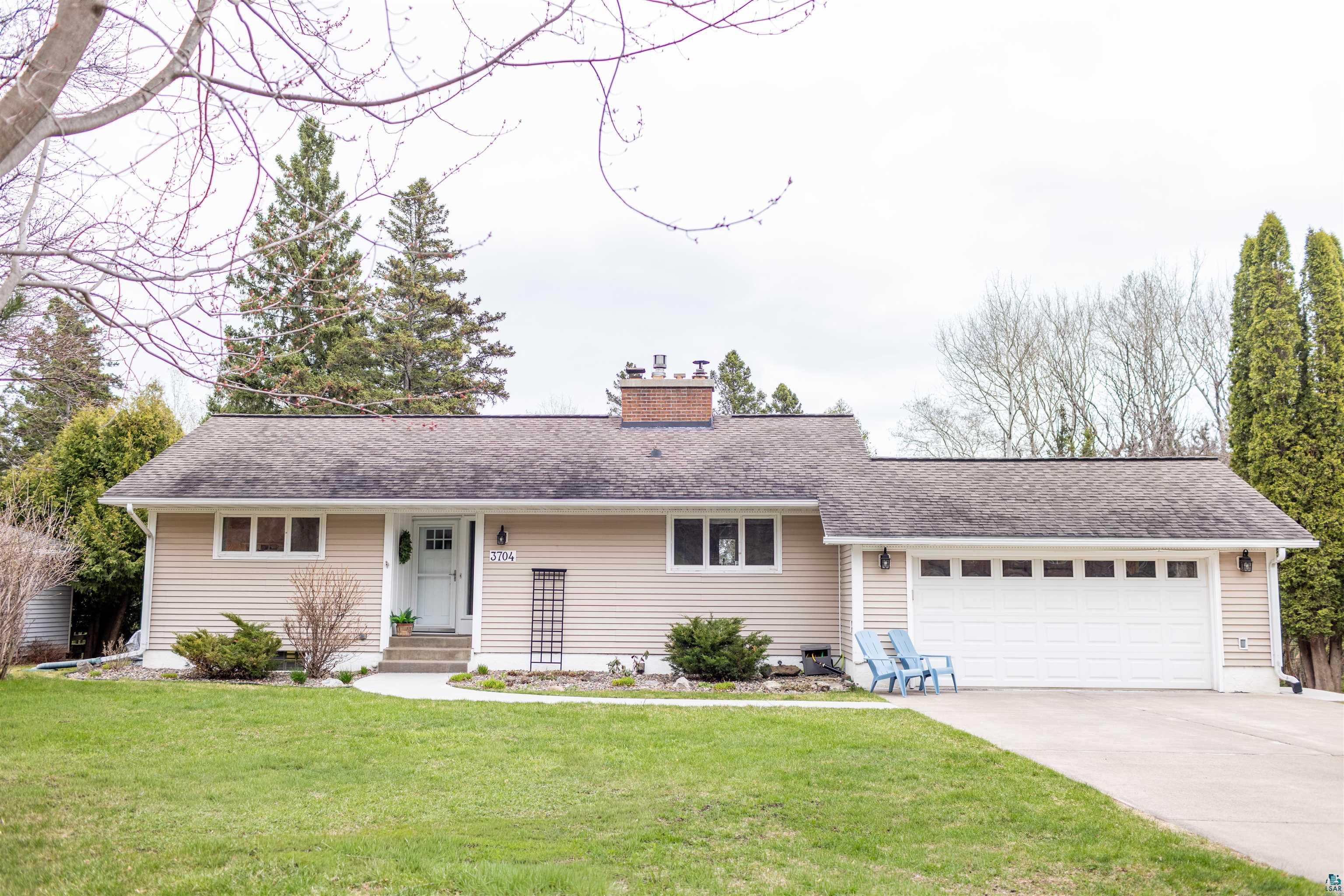 Ranch-style residence featuring horizontal siding, a two-car garage with paneling and windows, a front porch with concrete steps, and a brick chimney