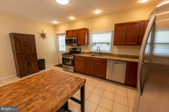 a kitchen with stainless steel appliances granite countertop a refrigerator a sink dishwasher a stove with wooden cabinets and floor