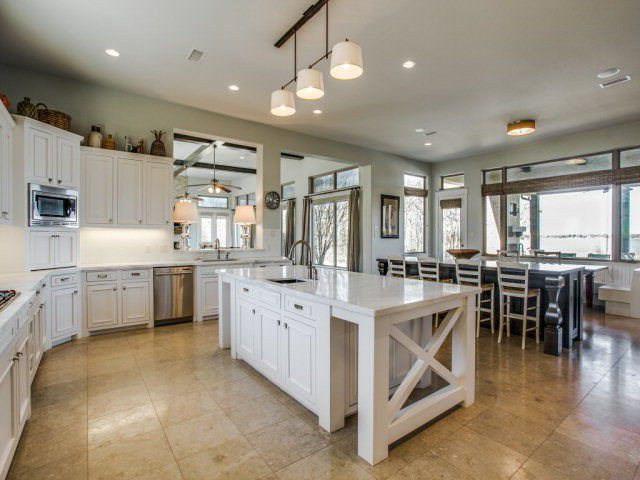 a large white kitchen with lots of counter top space a sink stainless steel appliances and cabinets