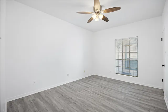 an empty room with wooden floor ceiling fan and windows
