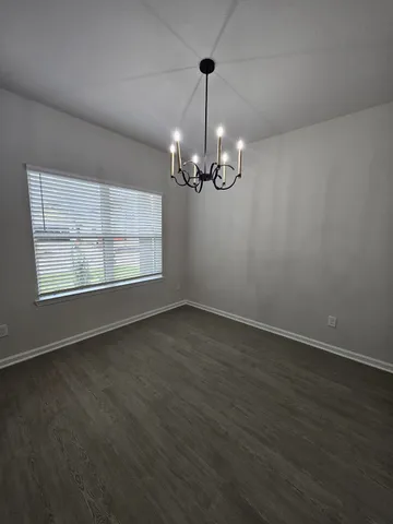 an empty room with wooden floor chandelier and windows