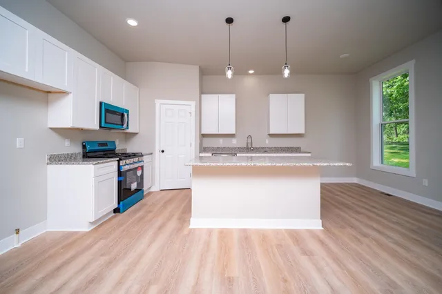 a large kitchen with granite countertop a large counter top a sink stainless steel appliances and cabinets