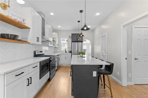 a large kitchen with stainless steel appliances kitchen island granite countertop a stove a sink a refrigerator and white cabinets with wooden floor