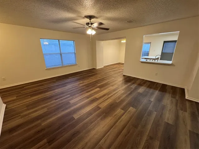 a view of an empty room with wooden floor and a ceiling fan