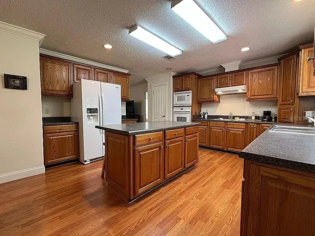 a kitchen with stainless steel appliances kitchen island granite countertop wooden floors and white cabinets