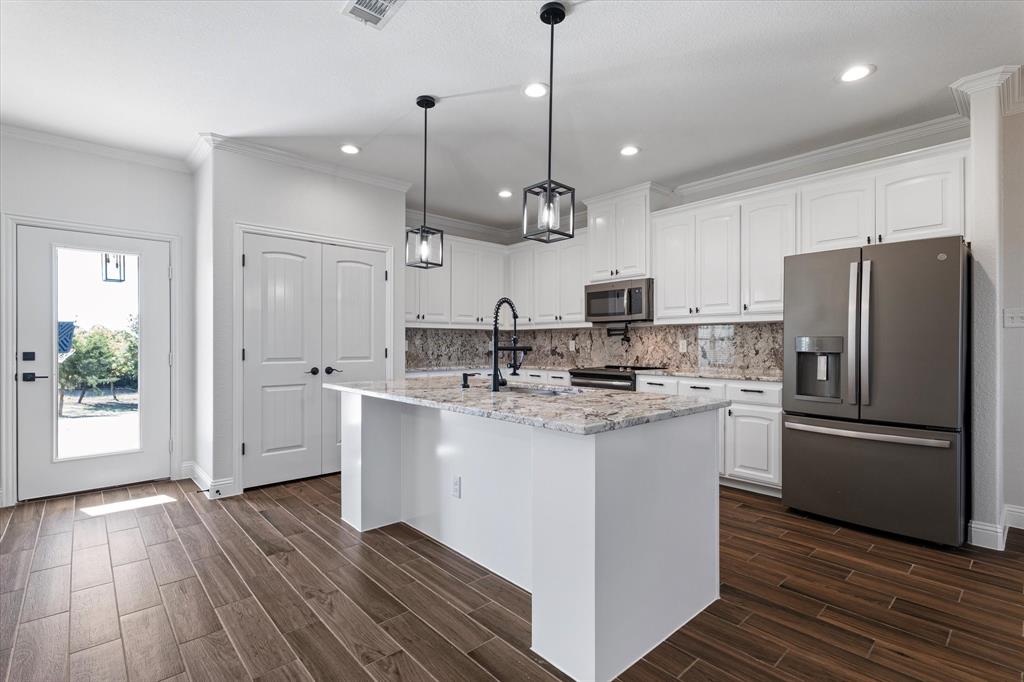 3511 West J E Woody Road Springtown, TX 76082 - Photo 11 of 34 Kitchen featuring appliances with stainless steel finishes, crown molding, white cabinets, light stone counters, and pendant lighting