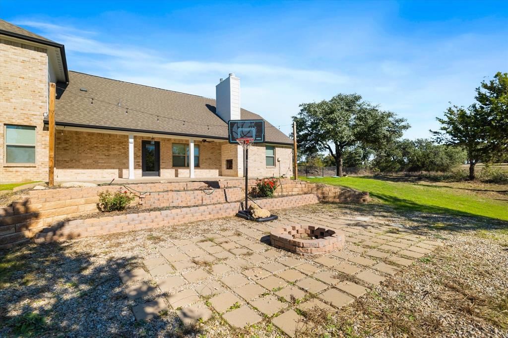 3511 West J E Woody Road Springtown, TX 76082 - Photo 30 of 34 Rear view of house with a patio area, a chimney, a fire pit, a lawn, and brick siding