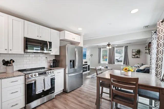 a kitchen with stainless steel appliances a stove a sink dishwasher a refrigerator white cabinets and wooden floor