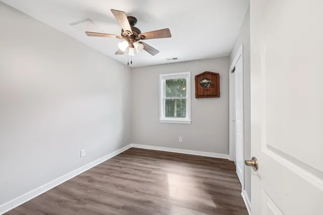 an empty room with wooden floor fan and windows