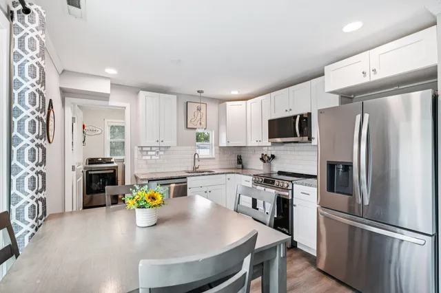 a kitchen with stainless steel appliances granite countertop a refrigerator a stove a sink dishwasher and white cabinets with wooden floor