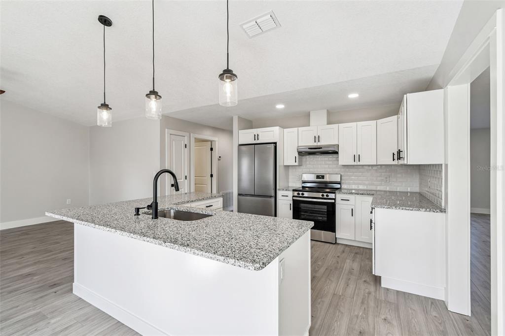 5248 Frost Road Spring Hill, FL 34606 - Photo 27 of 70 a kitchen with stainless steel appliances granite countertop a sink a stove a refrigerator and island with wooden floor