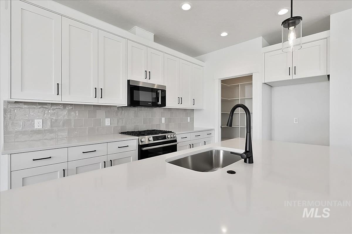 776 South Calhoun Lane Star, ID 83669 - Photo 12 of 49 Modern kitchen featuring a large island with an undermount sink, white shaker cabinetry with matte black hardware, stainless steel appliances, a gray subway tile backsplash, and recessed lighting
