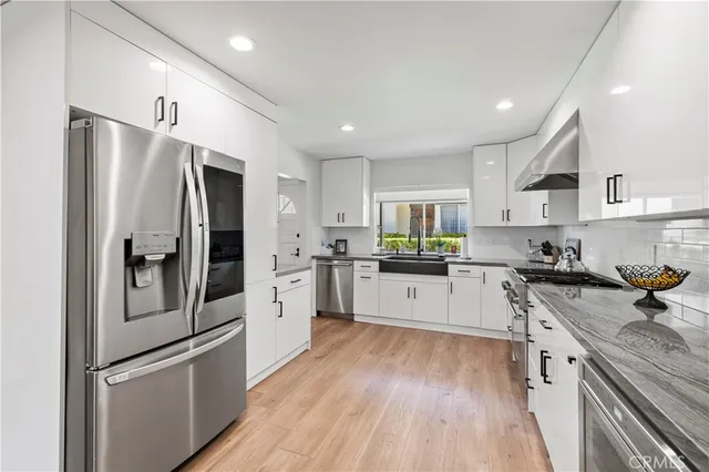 a kitchen with stainless steel appliances a refrigerator a sink and white cabinets