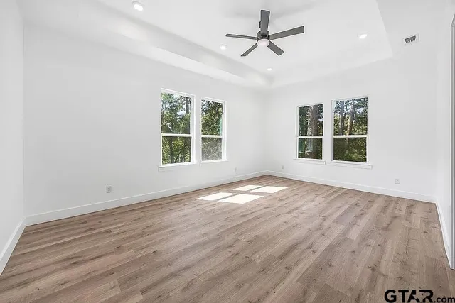 an empty room with wooden floor ceiling fan and windows
