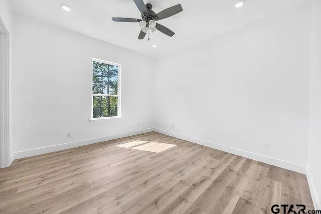 an empty room with wooden floor fan and windows