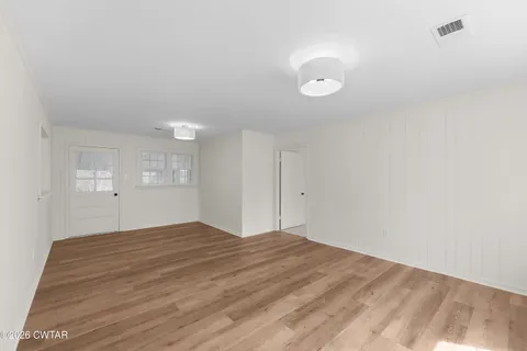 a view of an empty room with wooden floor and a window