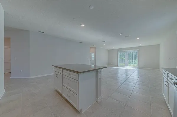 a view of an empty room with kitchen and window