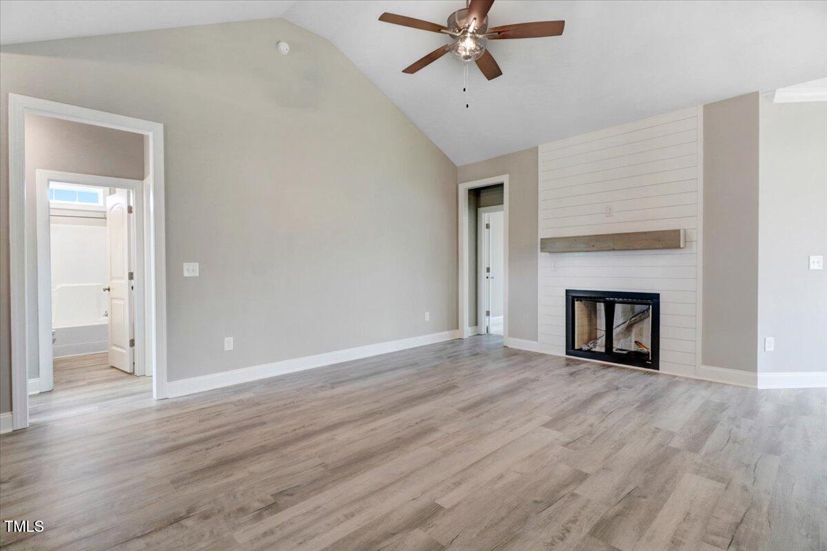 9550 Bear Run Lane Middlesex, NC 27557 - Photo 10 of 32 an empty room with wooden floor a ceiling fan a fireplace and windows