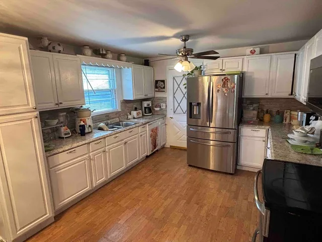 a kitchen with granite countertop a refrigerator a sink dishwasher a stove top oven a refrigerator and cabinets with wooden floor