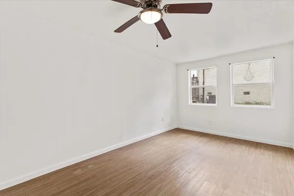 an empty room with wooden floor ceiling fan and window