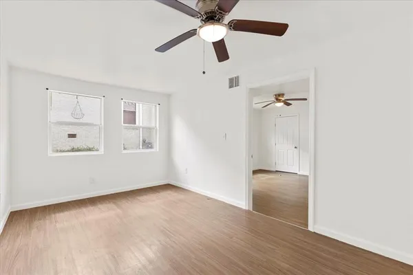 an empty room with wooden floor chandelier fan and windows