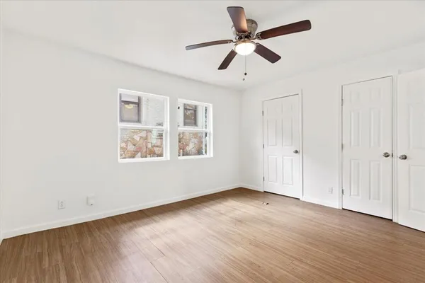 an empty room with wooden floor ceiling fan and windows