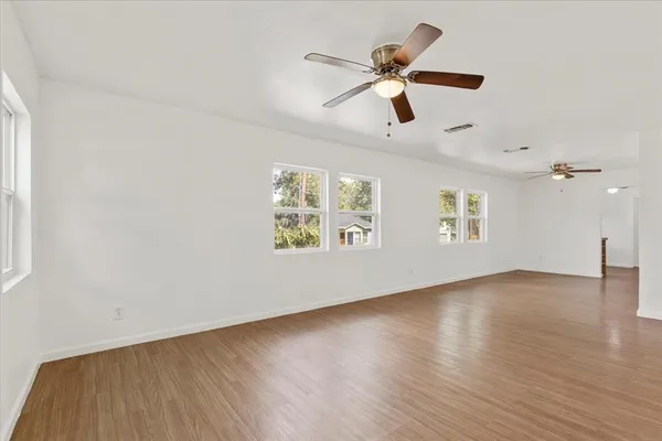 an empty room with wooden floor chandelier fan and windows