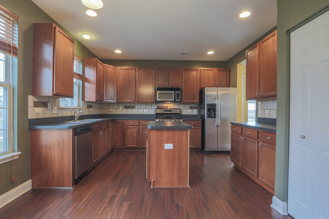 1240 Mariemont Road, Unit E Sugar Grove, IL 60554 - Photo 16 of 32 a kitchen with kitchen island granite countertop wooden floors stainless steel appliances a sink and a refrigerator