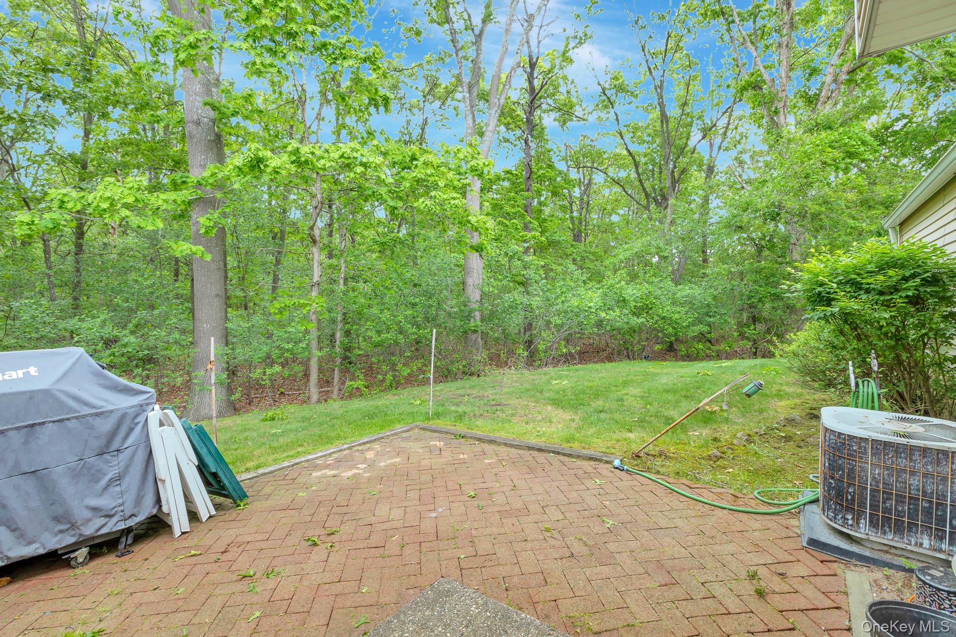 17 Stone Commons Yaphank, NY 11980 - Photo 29 of 31 Brick paver patio extending to a grassy yard surrounded by mature trees