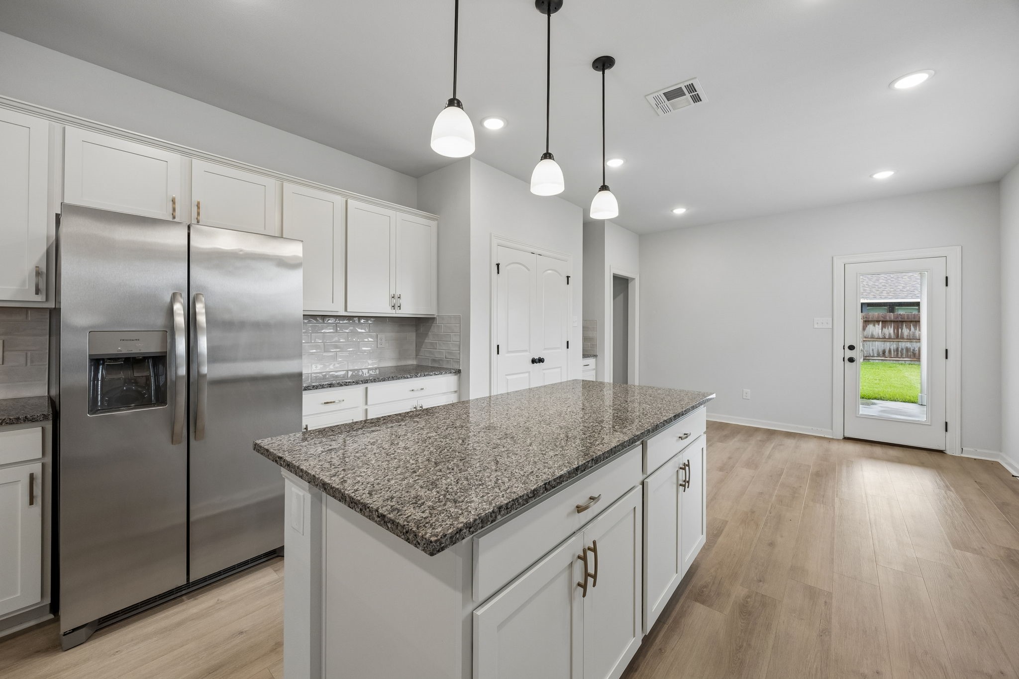 10902 Bonfire Trail Beasley, TX 77417 - Photo 11 of 36 This modern kitchen features stainless steel appliances, granite countertops, and white cabinetry. It includes a spacious central island, pendant lighting, and a door leading to the backyard, all set on elegant vinyl plank flooring.