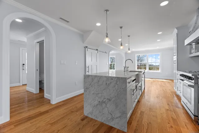 a large hall with kitchen island granite countertop a large counter top space a sink stainless steel appliances and cabinets