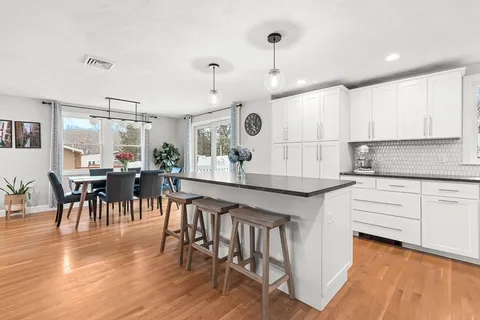 a kitchen with granite countertop a stove a sink a dining table and chairs with wooden floor