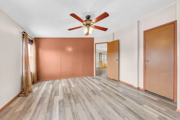 a view of an empty room with wooden floor and a ceiling fan