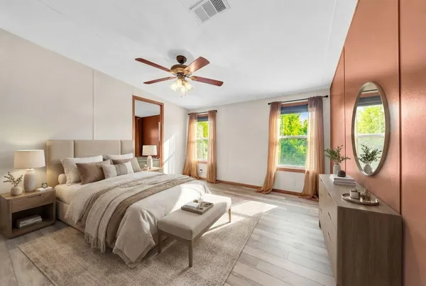 a spacious bedroom with a bed a mirror on the dresser and a window