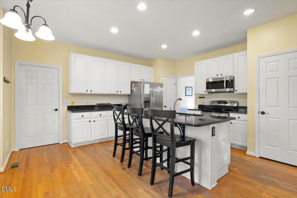 6512 Cablewood Drive Raleigh, NC 27603 - Photo 12 of 41 a kitchen with stainless steel appliances granite countertop a stove a sink a microwave a refrigerator and white cabinets with wooden floor
