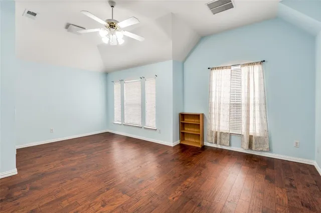 an empty room with wooden floor chandelier fan and windows