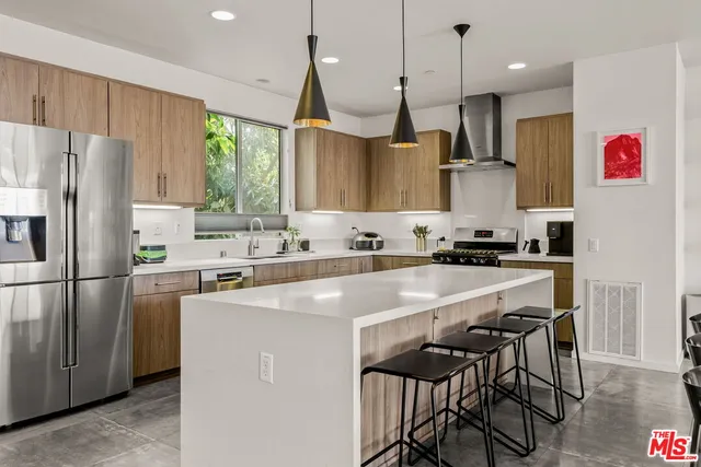 a kitchen with stainless steel appliances granite countertop a sink a stove a refrigerator and island with wooden floor