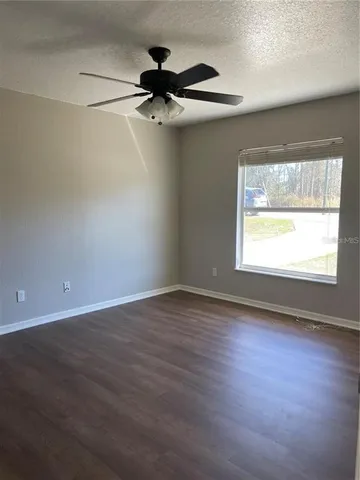 an empty room with wooden floor fan and windows