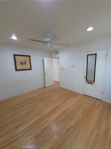 a view of an empty room with wooden floor and a ceiling fan