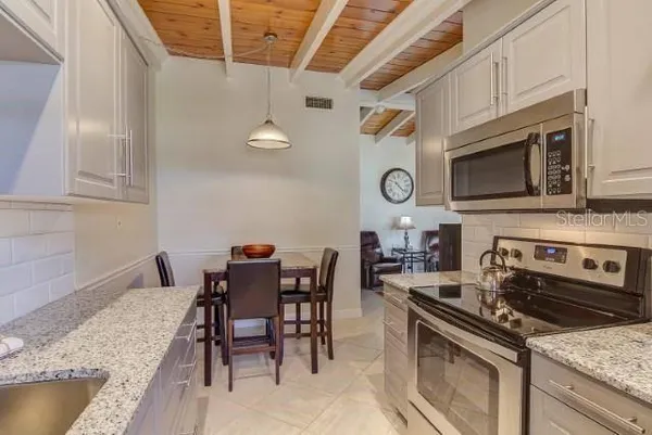 a kitchen with stainless steel appliances granite countertop a stove top oven a sink a dining table and chairs with wooden floor