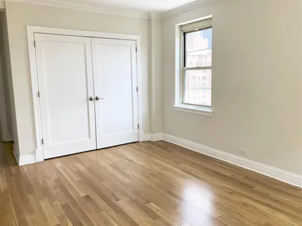 an empty room with wooden floor closet and windows