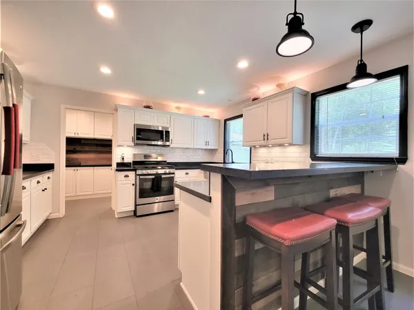 a kitchen with stainless steel appliances granite countertop a stove top oven a refrigerator a sink and chairs