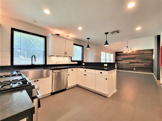 a large white kitchen with stainless steel appliances granite countertop a stove a sink a refrigerator and white cabinets with wooden floor