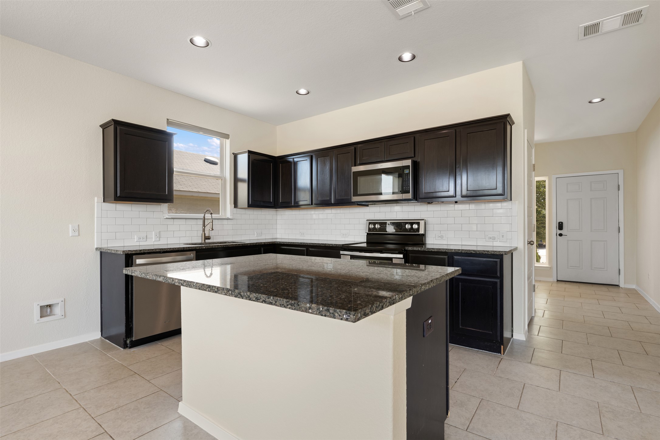 104 Cates Cove Elgin, TX 78621 - Photo 12 of 31 Dark cabinetry and granite countertops frame a central island in this open-concept kitchen.