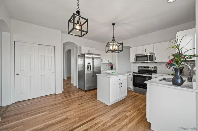 a kitchen with stainless steel appliances granite countertop a refrigerator a stove oven a sink dishwasher and white cabinets with wooden floor